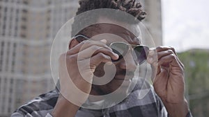 Close up face of confidient African American man standing against the background of urban building squinting in the sun