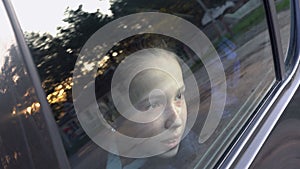 Close-up of the face of a cute little girl who looks thoughtfully through the glass of the car at the sky and sunset