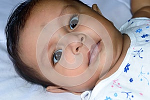 Close up face of cute newborn baby boy with black eyes posing at camera. One month old Sweet little infant toddler Closeup