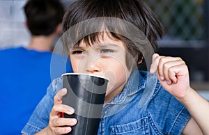 Close up face Cute toddler boy drinking cold drink, Happy Child sitting in cafe drinking soda or soft drink from paper cup,