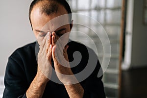 Close-up face of depressed male sitting alone at home holding face with hand, deep thoughts feeling lonely. Frustrated