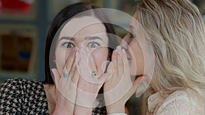 Close-up face of excited young woman with surprised facial expression listening friend whispering on ear. Portrait of