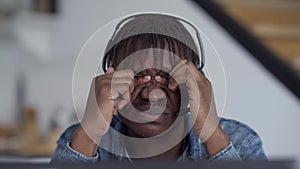 Close-up face of exhausted young man rubbing eyes in slow motion sitting at table with laptop in home office