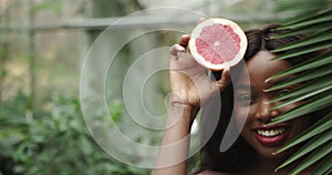 Close up of face and eyes of young beautiful african american woman, dark skin. Holding half of grapefruit close to her