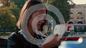 Close-up face of focused attractive woman reading on her smartphone, looking at camera and smiling.