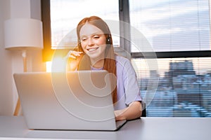 Close-up face of friendly young woman operator using headset and laptop during customer support at home office.
