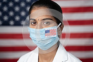 Close up face of Girl with I voted by main sticker on her medical mask with US flag as background - Concept of mail in voting in