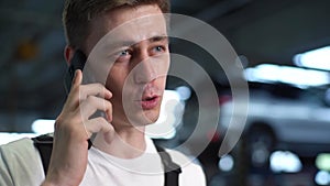 Close-up face of handsome cheerful mechanic male talking on mobile phone standing in auto repair shop garage with