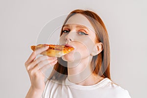 Close-up face of happy attractive young woman with appetite eating delicious pizza looking at camera standing on white