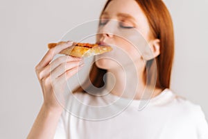 Close-up face of happy attractive young woman with closed eyes appetite eating delicious pizza standing on white