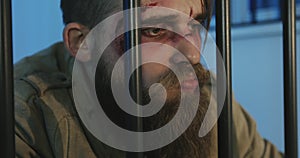 Close-up face of a homeless man with a beard in the prison cell.