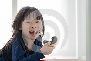 Close up face of hungry little Beautiful Asian girl eating chocolate donut, Cute kid eating donus with yummy face, Child eaitng