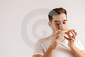 Close-up face of hungry young man enjoying sniffing slice of pizza and eating on delicious food on white isolated