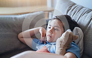 Close up face little boy sitting on sofa watching TV, Positive Kid lying on couch with dog toy in living room. Child relaxing at