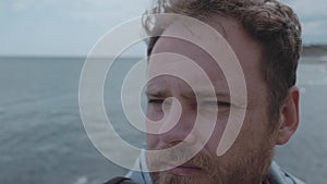 Close-up of the face of a man with a beard against the background of the sea and clouds. wind develops hair in a man 4k. 4k video