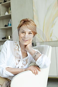 Close up face of a mature woman smiling and looking at camera. Retired woman in casuals sitting at home