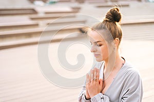 Close-up face of meditative young woman practicing yoga performing namaste pose with closed eyes outside in city park.