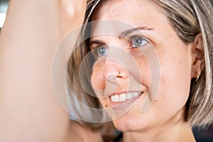 Close-up on the face of a mid adult smiley woman in an eagle pose during her yoga practice indoors