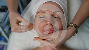 A close-up of the face of an older woman being massaged by a cosmetologist.