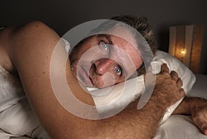 Close up face portrait of sleepless and awake attractive man with eyes wide open at night lying on bed suffering insomnia sleeping