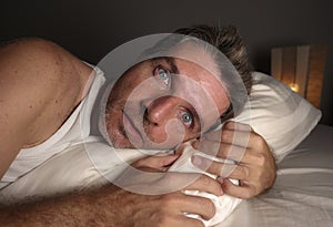 Close up face portrait of sleepless and awake attractive man with eyes wide open at night lying on bed suffering insomnia sleeping