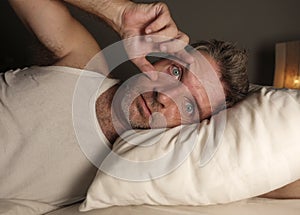 Close up face portrait of sleepless and awake attractive man with eyes wide open at night lying on bed suffering insomnia sleeping