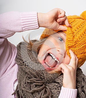 Close up face portrait of toothy smiling young woman wearing knitted hat and scarf.