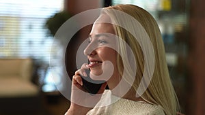 Close-up face of positive charming young woman laughing talking on smartphone in cafe. Happy blonde female having phone