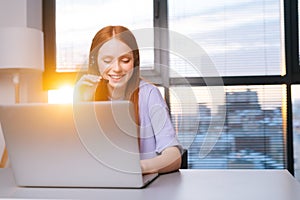 Close-up face of positive young woman operator using headset and laptop during customer support at home office.
