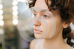 Close-up face of pretty brunette young woman with new wavy hairstyle looking in mirror with serious expression checking