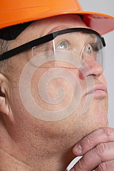 Close-up face profile of plump foreman in protective glasses thinking in doubts,construction worker in hard hat on studio