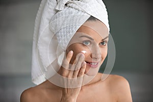 Beautiful 35s woman applying face cream after shower at home photo