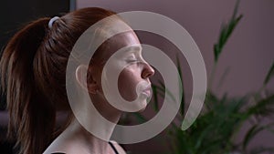 Close-up face of relaxed young woman doing breathing yogic practices at home, side view.