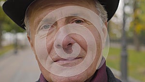 Close-up face of a senior Caucasian man with hazel eyes and grey hair looking at the camera. Mature guy standing in the