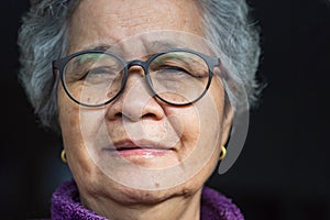 Close-up of face senior woman with short gray hair, wearing glasses, smiling and looking at the camera. Concept of aged people