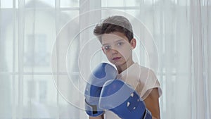 Close-up face of serious Caucasian boy standing in boxing stance. Brunette cute schoolboy wearing boxing gloves. Young