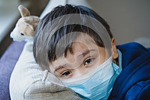 Close up face of Sick child wearing a protective mask, ill child in medical face mask lying head on sofa with sad face,Upset boy