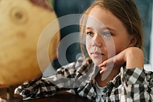 Close-up face of smiling curious child girl spinning small globe with interest, looking at countries of world.