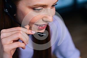 Close-up face of smiling young woman operator using headset during customer support at home office.