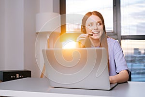 Close-up face of smiling young woman operator using headset and laptop during customer support at home office.