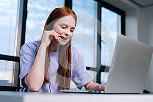 Close-up face of smiling young woman operator using headset and laptop during customer support at home office.