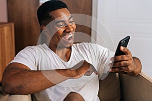 Close-up face of surprised African-American man receiving good news using mobile phone at home.