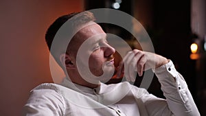 Close-up of face of thoughtful handsome young bearded man sitting in soft armchair at home.