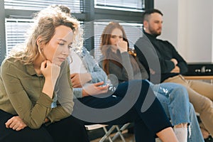 Close-up face of tired young Caucasian woman waiting job interview in queue line row in modern office lobby