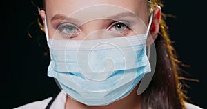 Close-up face of a woman wearing a protective medical face mask looking at the camera Head portrait of female doctor