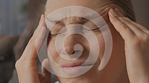 Close-up of the face of a woman who is worried about migraines. The woman rubs her head with her hand.