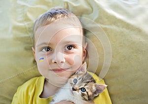 close-up of the face of a 3-year-old boy with a painted flag of Ukraine on his cheek and cute kitten muzzle