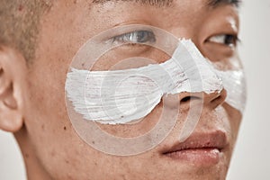 Close up of face of young asian man with problematic skin and hyperpigmentation applied mask on his face, looking away