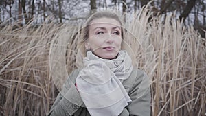 Close-up face of young beautiful Caucasian woman with brown eyes standing in cold wind. Charming blond girl waiting