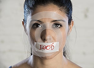 Close up face of young beautiful sad latin woman with mouth sealed on stick tape with the text no food